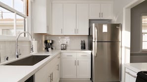 A modern kitchen with white cabinets, stainless steel appliances, and a large window providing natural light. - Universal Hideaway  (Burbank)