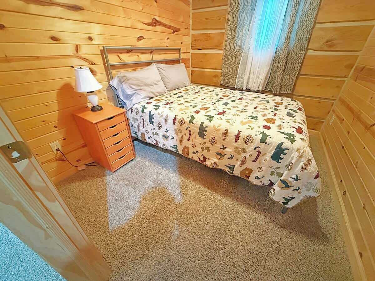 Una camera in una baita di legno con un letto, un comodino e una lampada.