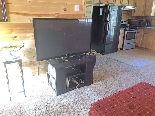 Ein Wohnzimmer mit Flachbildfernseher, einer schwarzen Unterhaltungsanlage, einem Kühlschrank und einer Küchenzeile mit Mikrowelle und Backofen.