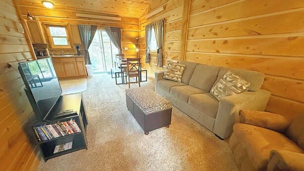 Ein gemütliches Blockhauskabinen-Interieur mit einer Couch, einem Hocker und einem Bücherregal mit DVDs.