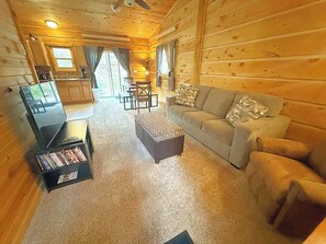 Ein gemütliches Blockhauskabinen-Interieur mit einer Couch, einem Hocker und einem Bücherregal mit DVDs.