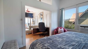 Un dormitorio con una cama grande, un escritorio y una silla. Se ve un ventanal con vistas al exterior.