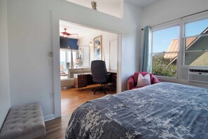 Ein Schlafzimmer mit einem großen Bett, einem Schreibtisch und einem Stuhl. Ein Fenster bietet Blick ins Freie.