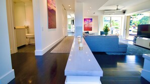 Una sala moderna con una larga mesa de centro blanca, un sofá gris y un televisor sobre un mueble blanco.