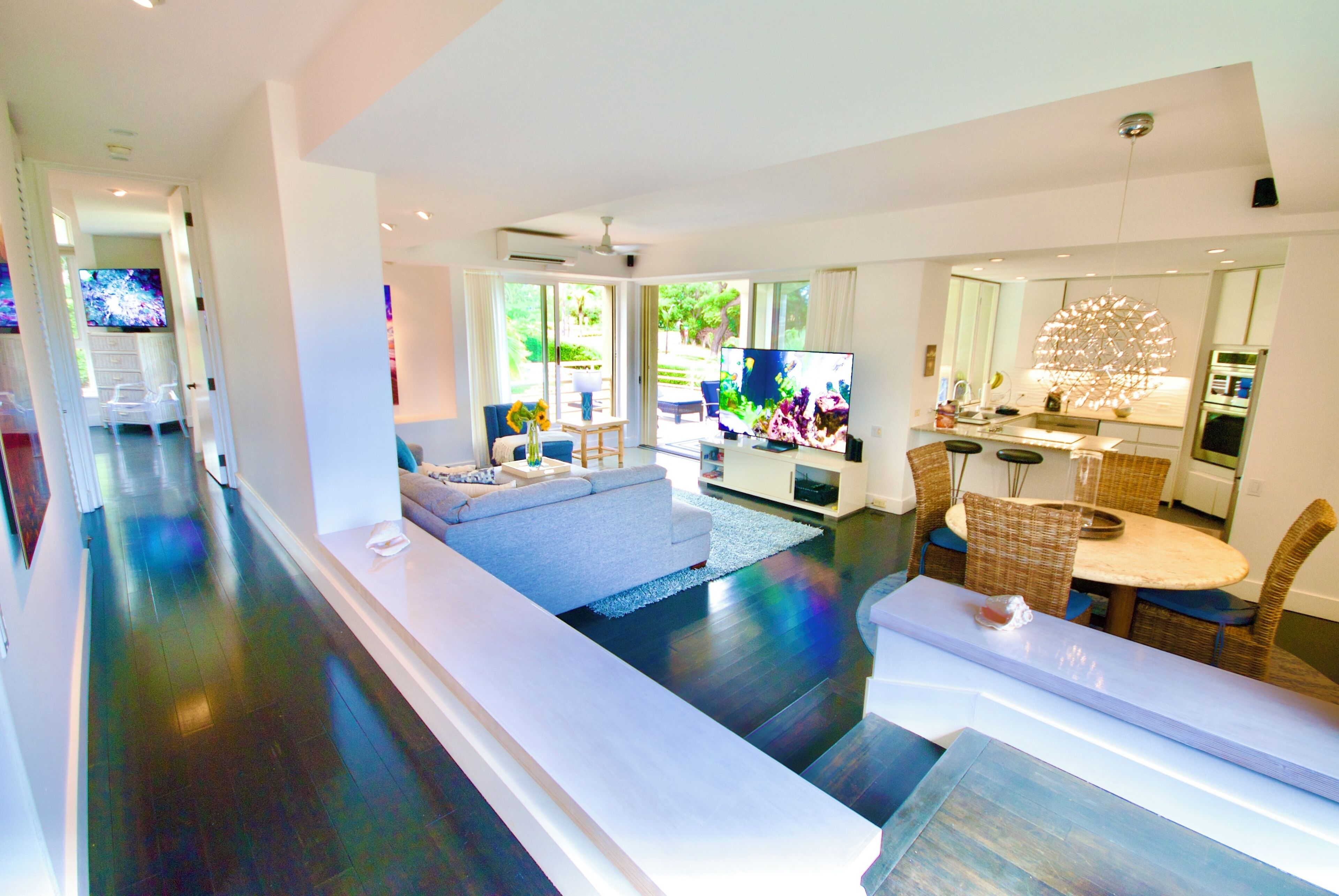 A modern living room with a sofa, TV, dining area, and kitchen.