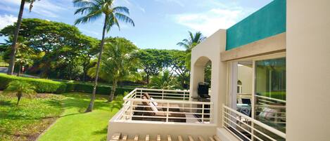 A balcony with a wooden railing overlooking a well-maintained lawn and palm trees.