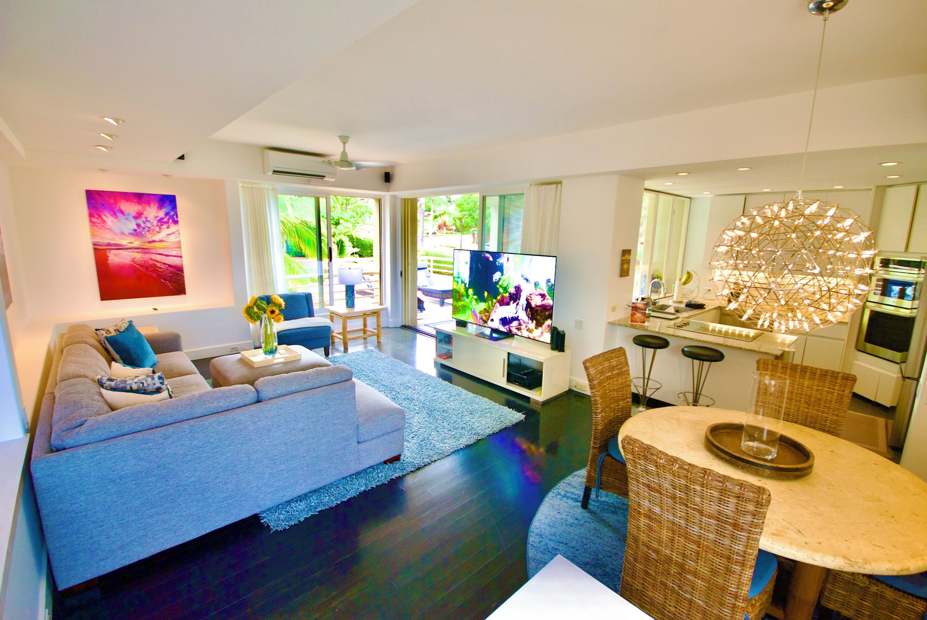 A modern living room with a sofa, a dining area with a round table, and a kitchen with a unique light fixture.