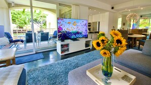 Una sala moderna con televisor de pantalla plana, un sofá, una mesa de centro con una bandeja y un florero con girasoles.
