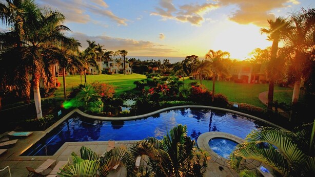 Zona de piscina en un resort, con vista al océano y un campo de golf al fondo.