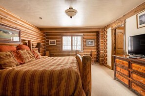 Un dormitorio tipo cabaña de troncos con una cama grande, cabecera de madera y un aparador con cajones.