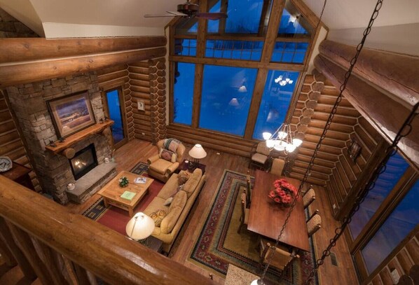 A log cabin interior with a fireplace, wooden furniture, and a large window offering a view. - Teton Springs Cabin with Private Hot Tub and Air Conditioning (Victor)