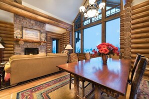 A log cabin interior with a fireplace, a sofa, a dining table, and a view through large windows. - Teton Springs Cabin with Private Hot Tub and Air Conditioning (Victor)
