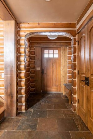 A log cabin interior with a stone-tiled floor, a wooden door, and a bench. - Teton Springs Cabin with Private Hot Tub and Air Conditioning (Victor)