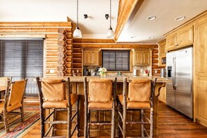 A rustic kitchen with wooden cabinets, a stainless steel refrigerator, and a bar area with stools. - Teton Springs Cabin with Private Hot Tub and Air Conditioning (Victor)