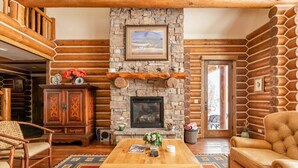 A cozy log cabin interior with a stone fireplace, wooden furniture, and a view through a glass door. - Teton Springs Cabin with Private Hot Tub and Air Conditioning (Victor)