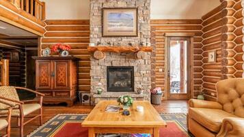 A cozy log cabin interior with a stone fireplace, wooden furniture, and a view through a glass door.