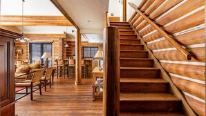 A wooden interior with a staircase, wooden floors, and a dining area with chairs and a table. - Teton Springs Cabin with Private Hot Tub and Air Conditioning (Victor)