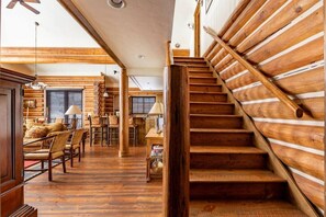 Un interior de madera con una escalera, pisos de madera y un comedor con sillas y una mesa.
