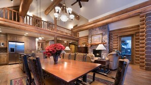 A spacious living room with a wooden dining table, comfortable seating, a fireplace, and a view of the outdoors. - Teton Springs Cabin with Private Hot Tub and Air Conditioning (Victor)