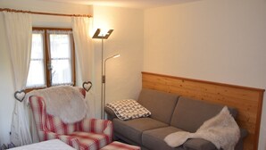 Et værelse med en seng, en rød ternet stol, en brun sofa og en gulvlampe.