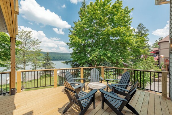 A wooden deck with Adirondack chairs and a table, overlooking a lake and forested area. - Deep Creek Gem w/ Dock, Fire Pit, Views & Hot Tub (Oakland)