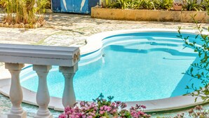 A swimming pool with a stone border, surrounded by plants and flowers.