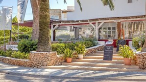 A restaurant with outdoor seating, stone walls, potted plants, and a clear view of the street.