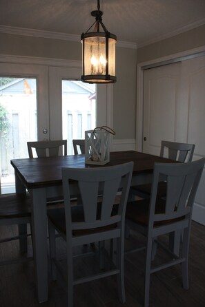 A dining area with a wooden table and white chairs, a hanging lantern, and a view of the outside through a door.