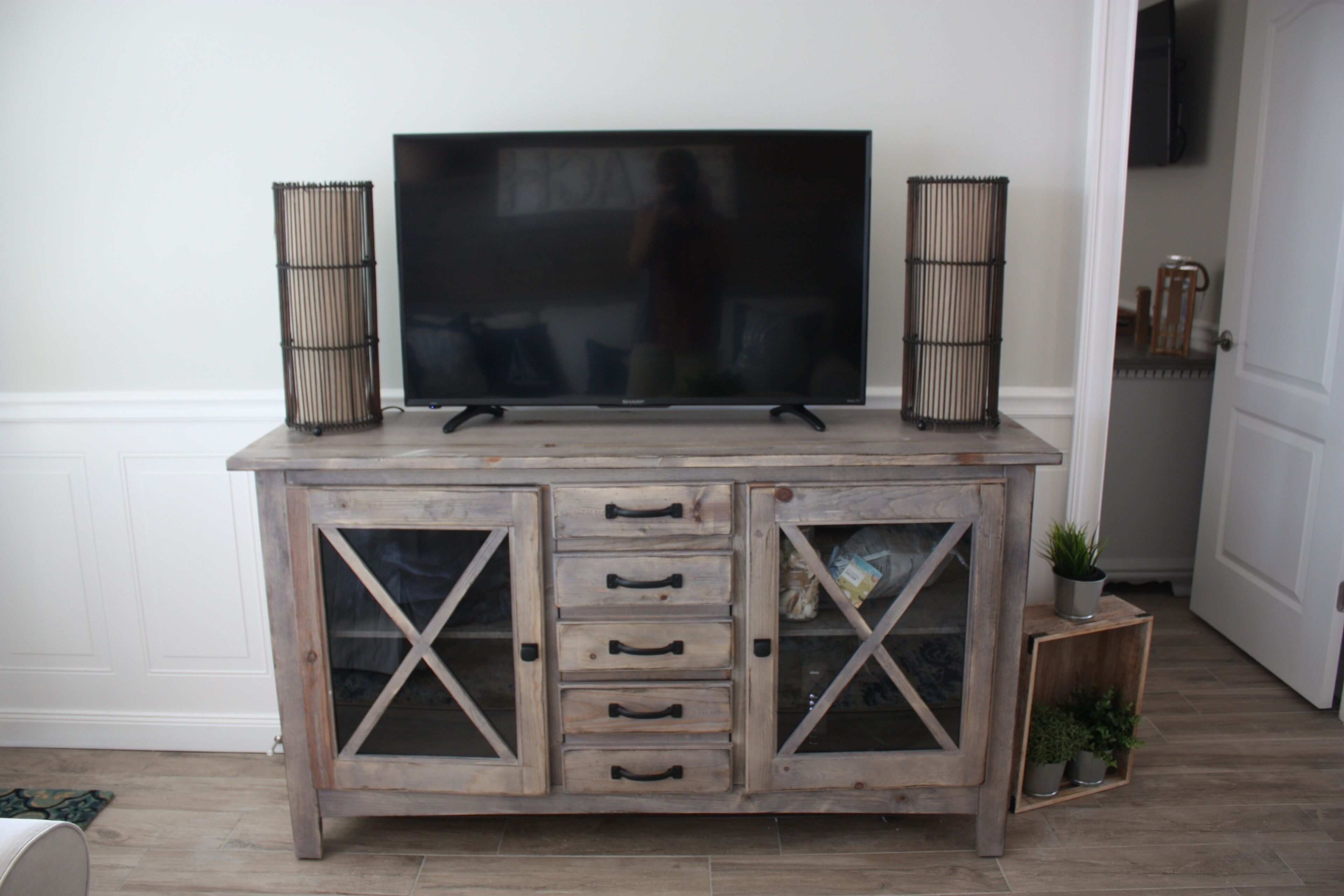 A wooden TV stand with a flat-screen TV, two decorative baskets, and a small plant.