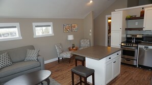 Cocina moderna con armarios blancos, una isla central y una zona de comedor con sofá gris y cojines estampados.