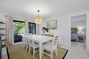 A modern dining area with a white table and chairs, a hanging light fixture, and a painting on the wall.