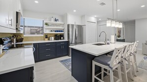A modern kitchen with dark blue cabinets, a large island, stainless steel appliances, and a white countertop.