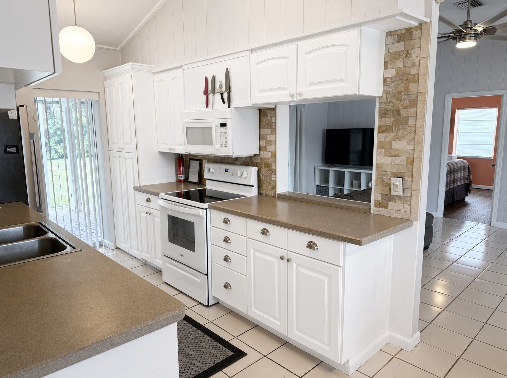 Une cuisine avec des meubles blancs, un four à micro-ondes, un four traditionnel et un mur décoratif en pierre.