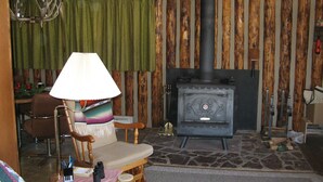 Una sala de estar acogedora con chimenea de piedra, una silla de madera, una lámpara y una mesa con diversos objetos.