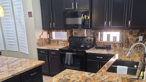 A kitchen with dark cabinets, a granite countertop, a built-in microwave, and a stainless steel sink.