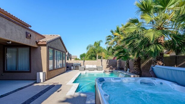 A backyard with a swimming pool, hot tub, and outdoor furniture.