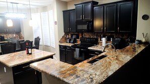 A modern kitchen with granite countertops, black cabinetry, and stainless steel appliances.