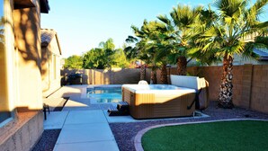 A backyard with a hot tub, a pool, and palm trees.
