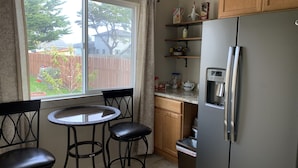 Una cucina compatta con frigorifero, un piccolo tavolo da pranzo con sedie e una finestra vista giardino.
