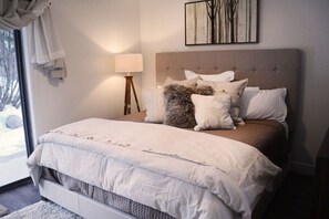 Une chambre avec un grand lit, une lampe de chevet, une fenêtre avec des rideaux et une œuvre d’art accrochée au mur.
