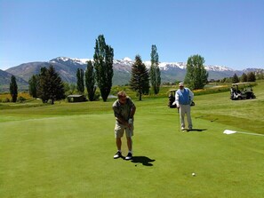 Un parcours de golf avec une chaîne de montagnes en arrière-plan, un chariot de golf et une personne qui s'apprête à effectuer un putt.