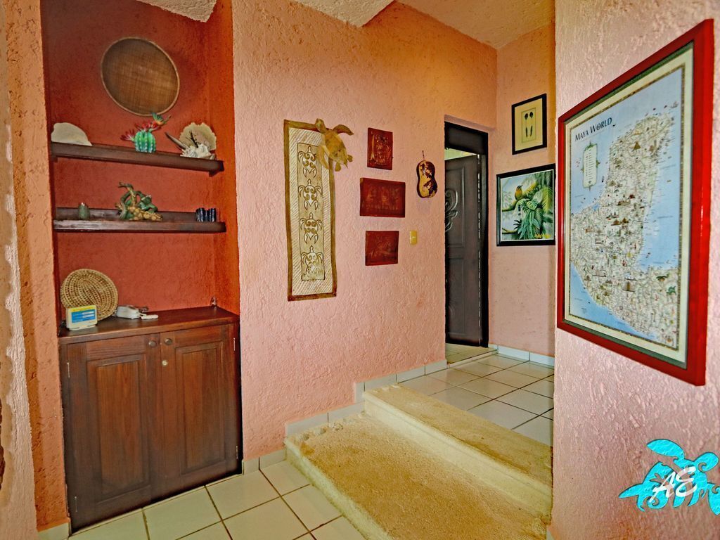 Un couloir avec un meuble en bois, des étagères ornées d’objets décoratifs, des tableaux encadrés et une carte accrochée au mur.