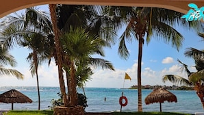 Une vue sur la plage, avec des palmiers, une bouée de sauvetage et un parasol en feuilles de palmier.