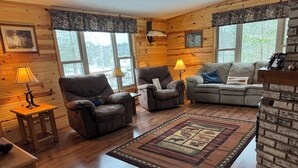 A cozy cabin-style living room with wooden walls, a fireplace, and a large window. - Little Muskie Retreat on Little Muskie Lake, Canoe included!   Snowmobile! (Woodruff)
