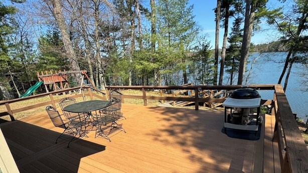 A wooden deck with a table and chairs, overlooking a lake and surrounded by trees. - Little Muskie Retreat on Little Muskie Lake, Canoe included!   Snowmobile! (Woodruff)