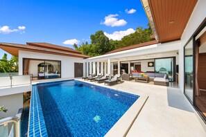 A modern pool area with a clear blue pool, sun loungers, and a covered seating area.
