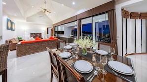 A dining area with a large table set for a meal, surrounded by chairs, and a sofa with orange cushions in the background.