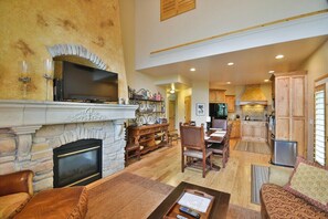 A spacious living room with a stone fireplace, a television, and a dining area with wooden furniture. - Large Townhome sleeps 16 with Private Hot Tub, Theater Room (Eden)