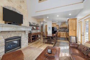 Una sala de estar amplia con chimenea, televisor montado en la pared, comedor con muebles de madera y cocina con armarios de madera.