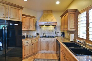 A kitchen with wooden cabinets, a stainless steel refrigerator, a gas stove, and a black sink. - Comfy Large Townhome with private hot tub (Eden)